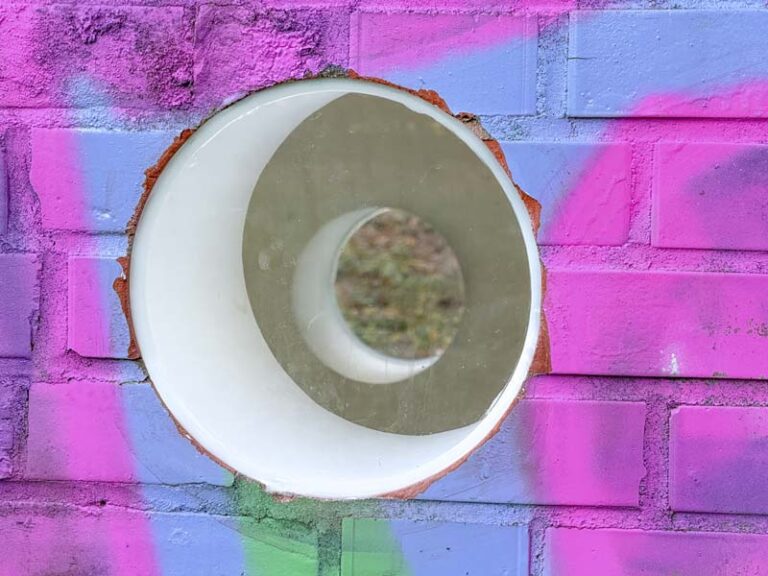 Nahaufnahme von verglastem Guckloch auf Wand mit Graffiti